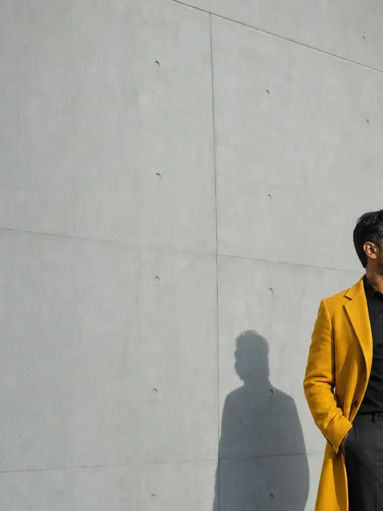Entrepreneurial mindset on display as a person in a bright yellow blazer stands beside a concrete wall, looking left with a shadow cast behind.